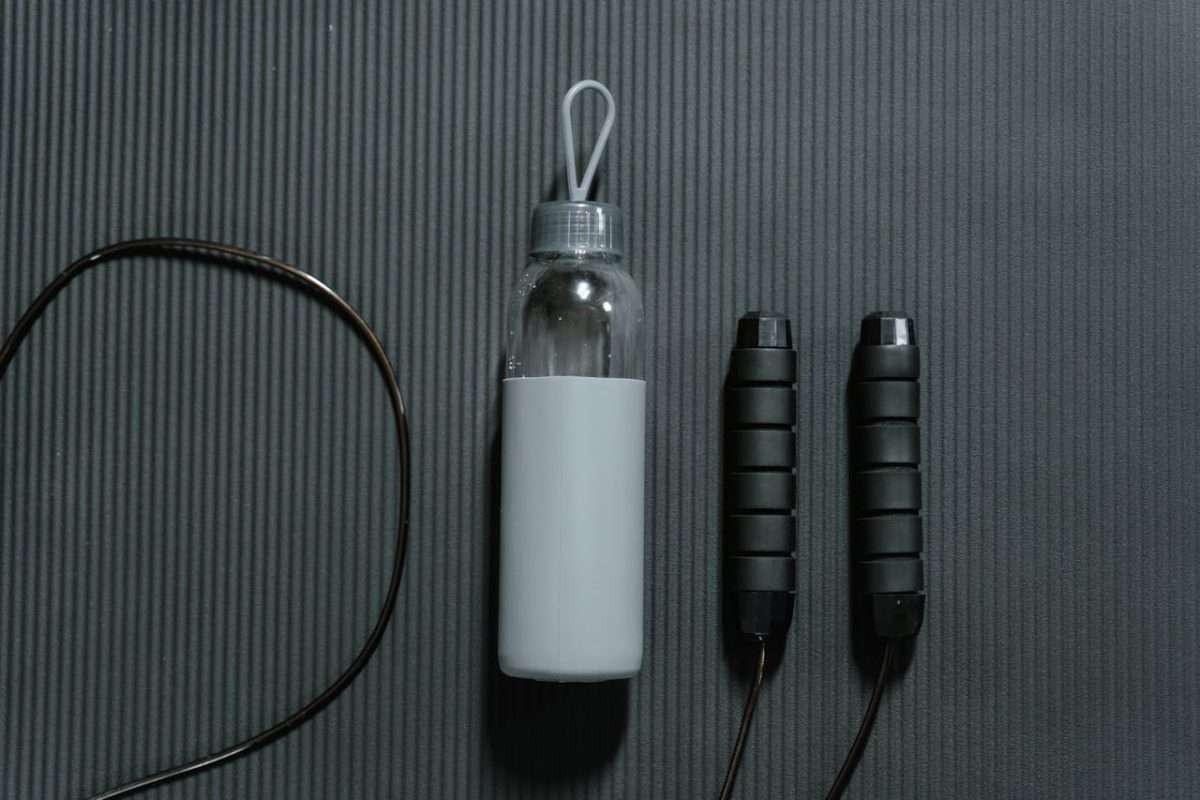 Flatlay of a water bottle and jump rope on a yoga mat, highlighting fitness essentials.